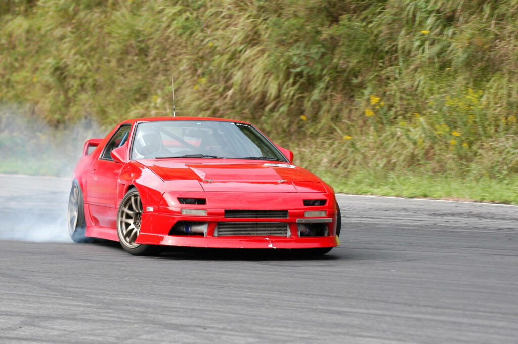 Red Mazda RX-7 Enveloped in White Smoke Amidst Lush Greenery - Dynamic RX7 Backdrop Wallpaper
