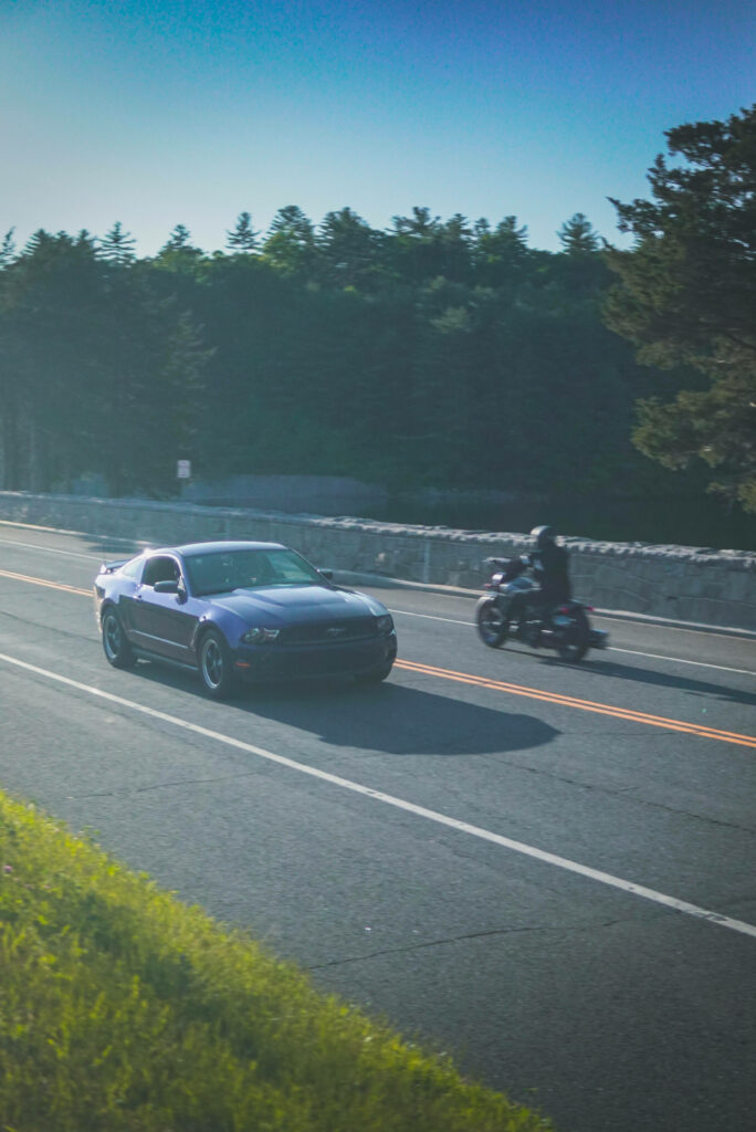 The Thrilling Encounter: Ford Mustang and Motorcycle Racing Amidst Enchanting Forest Scenery - Captivating iPhone Wallpaper