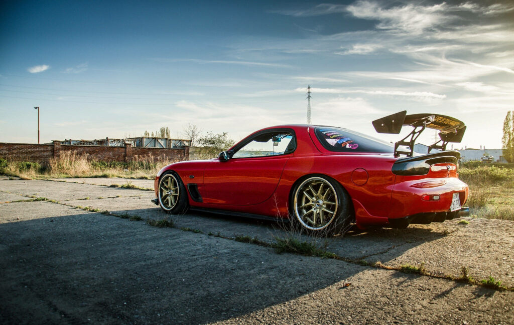 Vibrant Red Mazda Rx-7 with Sleek Rear Wing Showcased in Abandoned Brick Surroundings Wallpaper