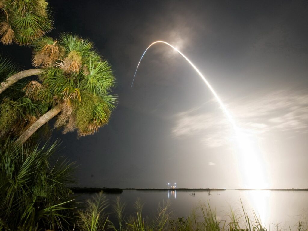 Rocket streaking over tropical sea with illuminated palm trees at sunset wallpaper background