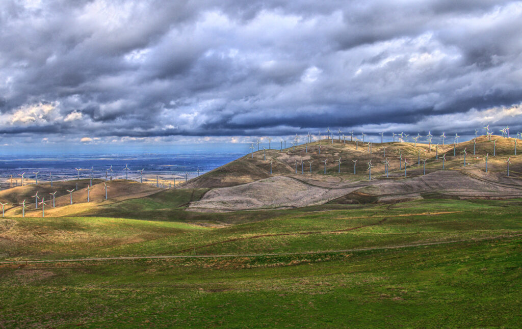 Rolling green hills with modern windmills under dramatic clouds and distant blue sea wallpaper
