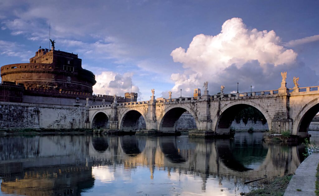 Roman Bridge of Castel Sant Angelo with stone arches statues reflected in calm river at sunset Wallpaper