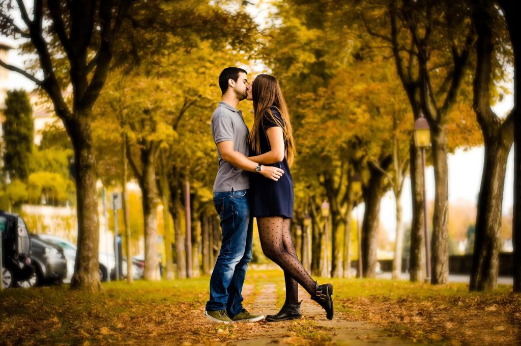 Couple sharing a romantic kiss on autumn path with golden trees warm intimate moment wallpaper