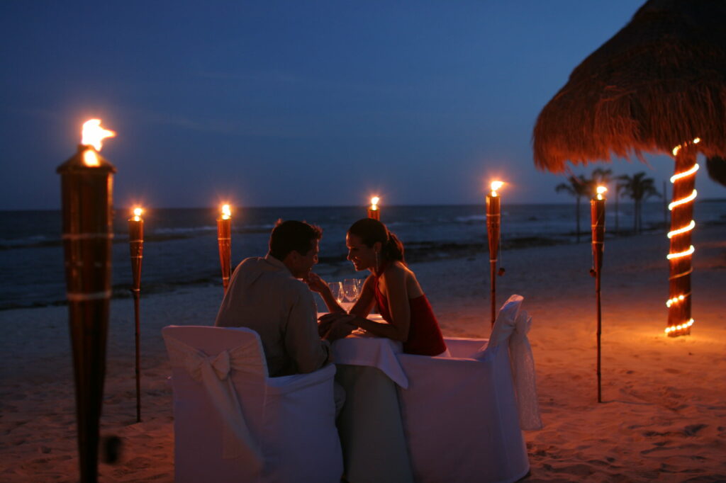 A Captivating Evening by the Sea: A Romantic Dinner Setting with Mesmerizing Sky, Twinkling Lights, and Ocean Serenade Wallpaper