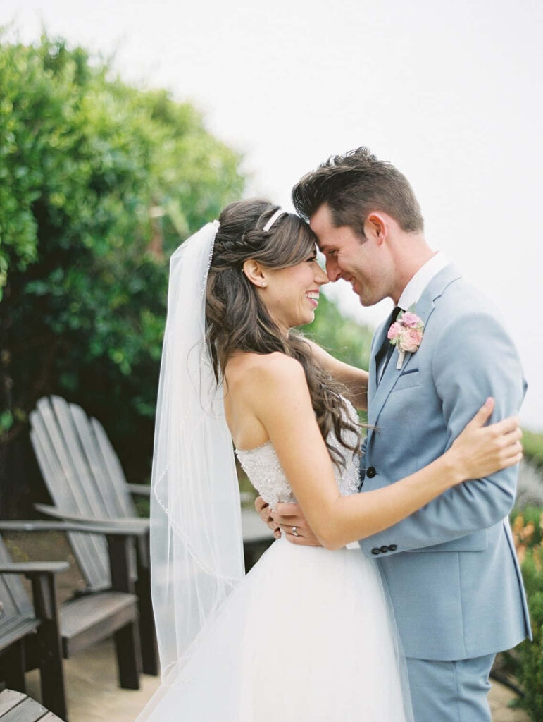 Bride in white gown and groom in blue suit share romantic moment outdoors with green backdrop Wallpaper