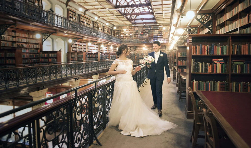 Bride and groom share romantic moment inside elegant Adelaide State Library with grand bookshelves Wallpaper