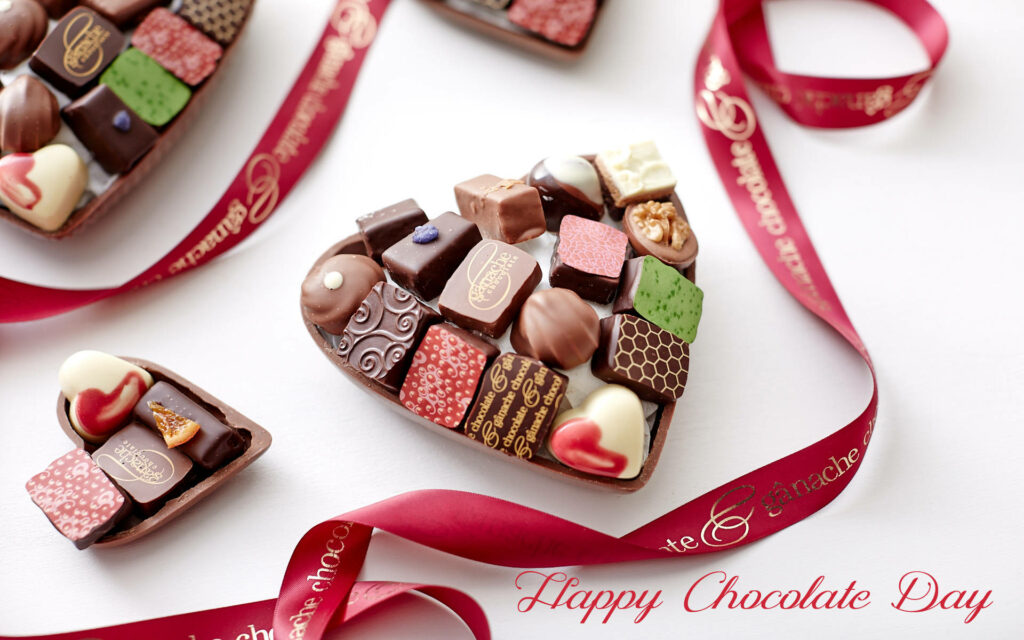 Heart-shaped assorted chocolates with red ribbon on white background Chocolate Day wallpaper