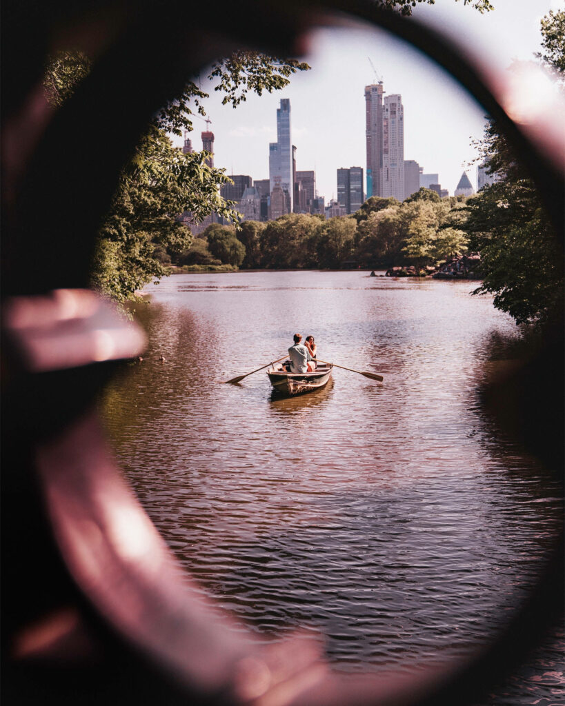 Romantic couple boating on calm Central Park lake with NYC skyline and lush greenery view Wallpaper