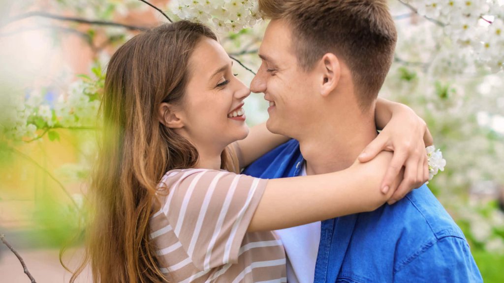 Happy couple embracing in blooming white flowers romantic wallpaper background with soft lighting