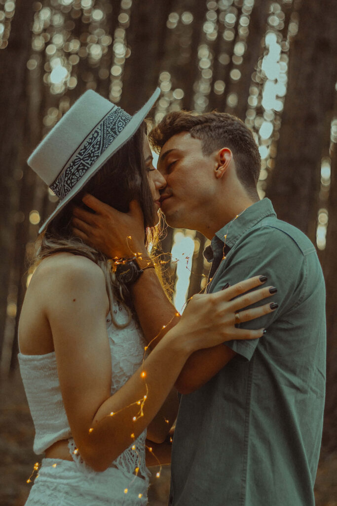 Romantic couple kissing under warm string lights in a dreamy forest setting wallpaper background