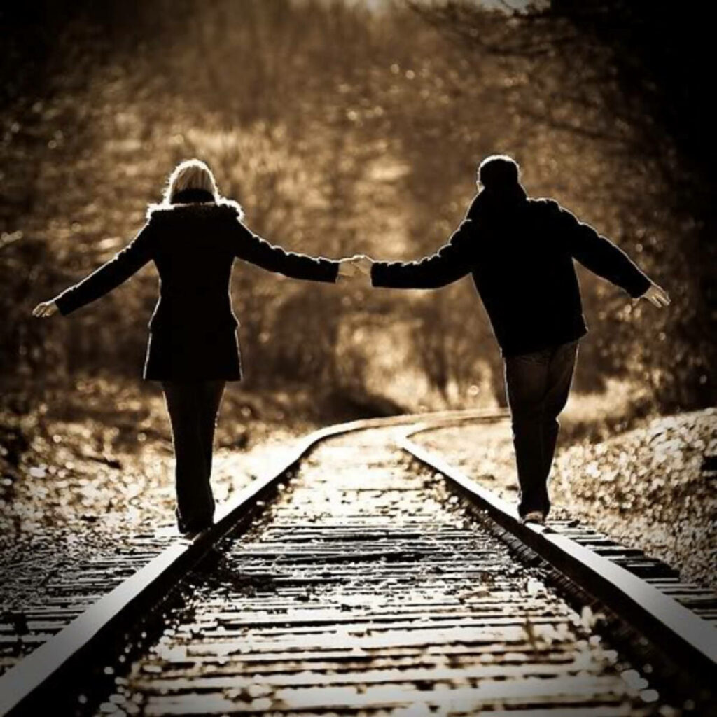 Perfectly Aligned: A Stylish Couple Defying Balance on Railway Wallpaper