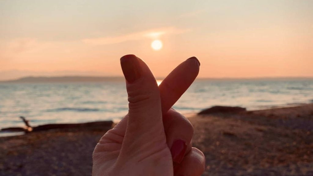 Romantic hand finger heart framing golden hour sunset over calm ocean and sandy beach Wallpaper
