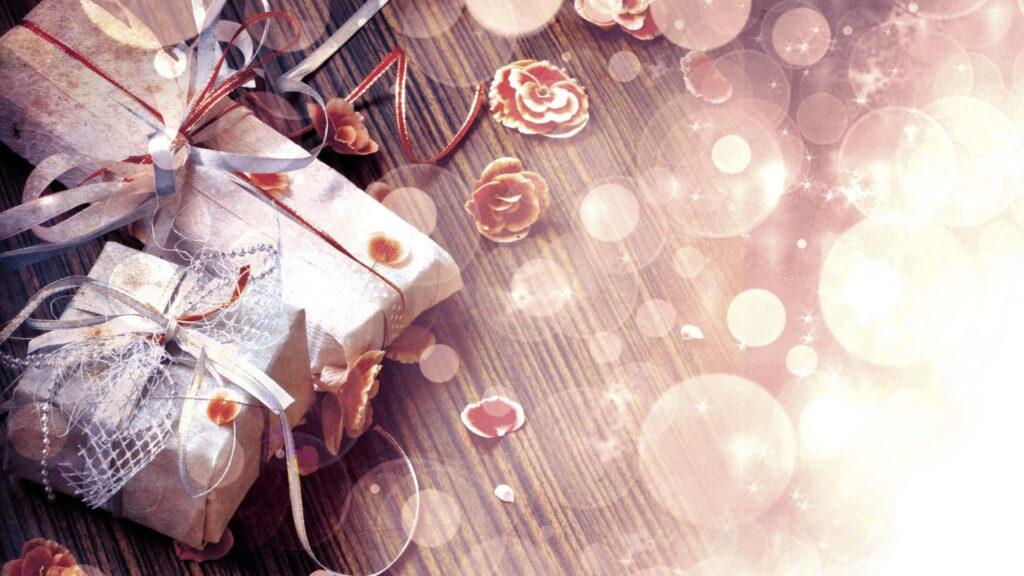 Beautifully wrapped gift with ribbons on rustic wood surrounded by rose petals and glowing bokeh Wallpaper
