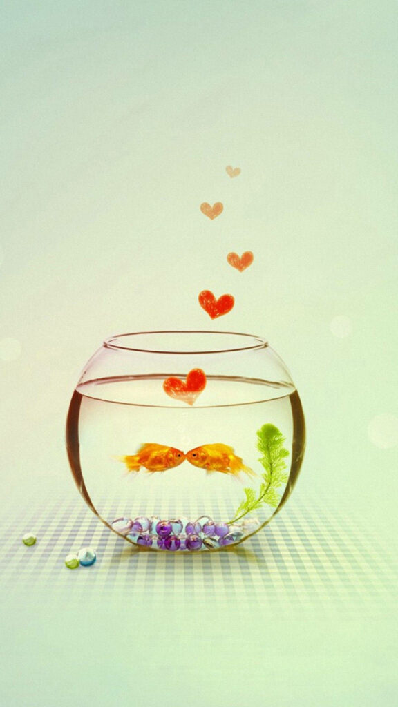 Two goldfish swim in a bowl with colorful pebbles and hearts creating a romantic scene Wallpaper