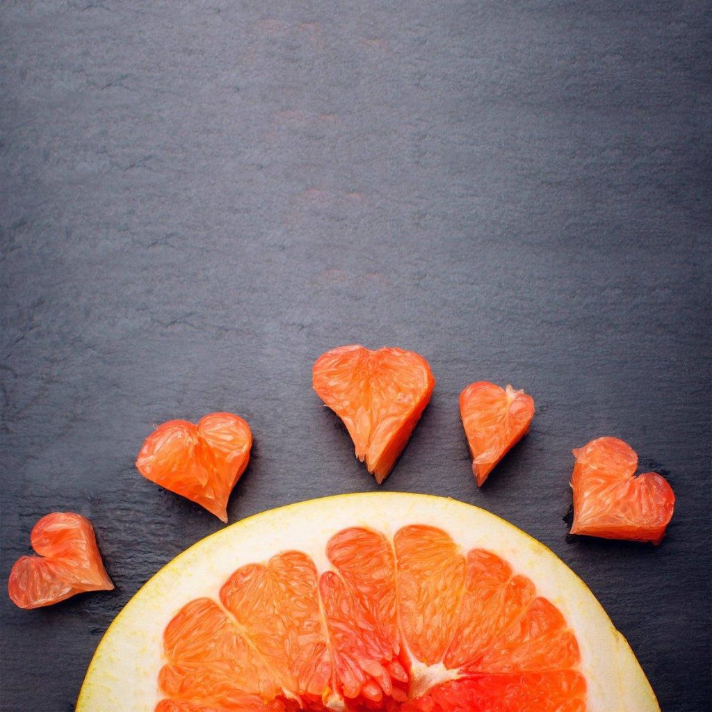 Fresh grapefruit slice with heart-shaped fruit segments on dark textured stone background wallpaper