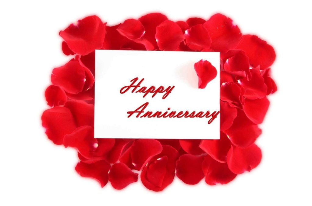 Happy Anniversary card with red cursive on white surrounded by fresh red rose petals wallpaper
