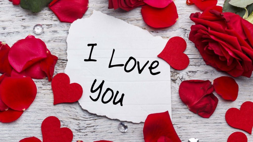Romantic I Love You note with red rose petals hearts and crystals on white wooden table wallpaper