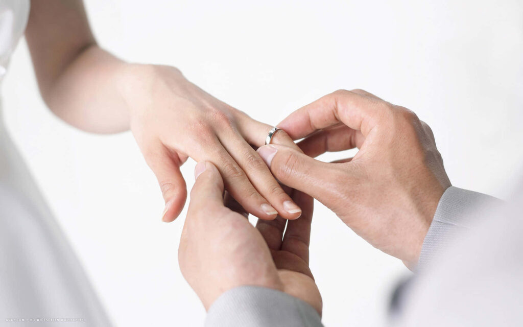 Romantic marriage proposal with husband placing ring on wife’s finger soft white background Wallpaper