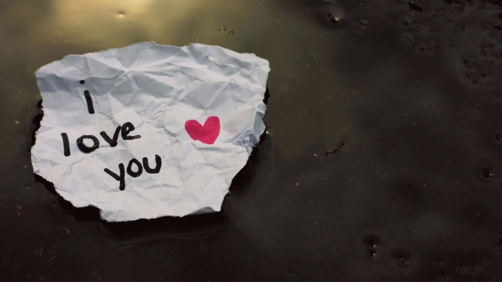 Crumpled white paper with handwritten i love you and pink heart floating on dark water Wallpaper