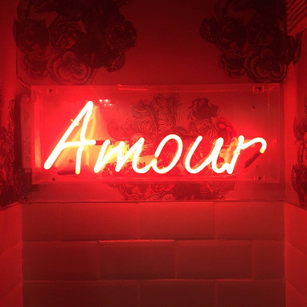 Red neon Amour sign on dark floral wallpaper with white subway tiles stylish background