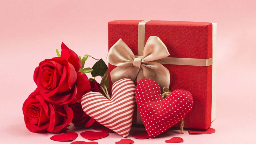 Red gift box with satin bow roses and heart decorations on soft pink romantic background Wallpaper