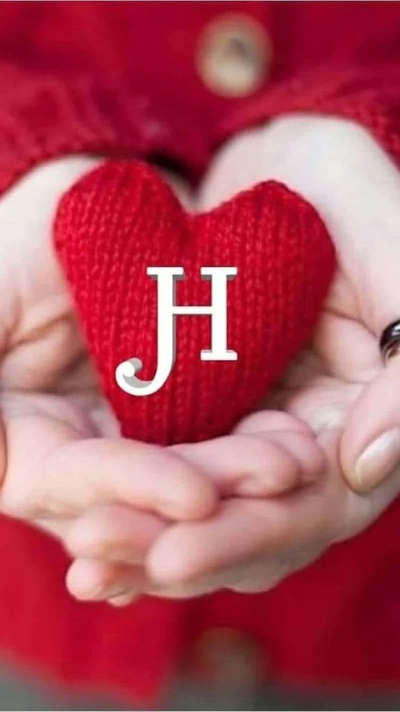 Hands holding a red knitted heart with white letter H on a warm romantic wallpaper background