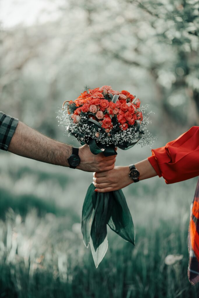 Romantic Wallpaper: Hands Holding Vibrant Red Roses & Lush Greenery