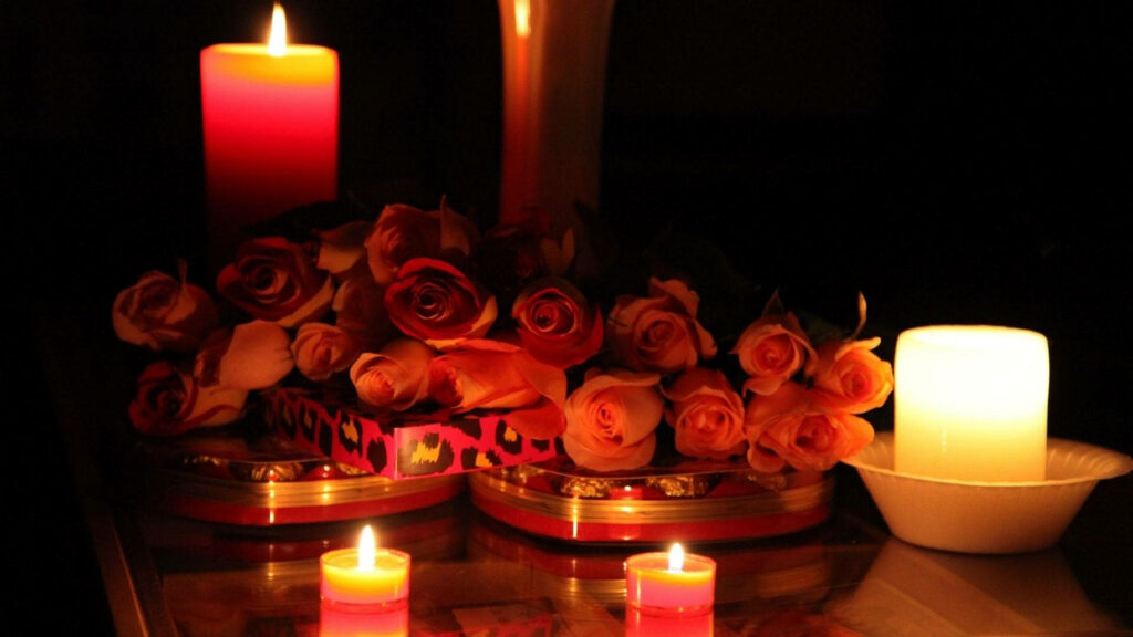 Romantic red and cream roses with glowing candles creating warm intimate wallpaper background