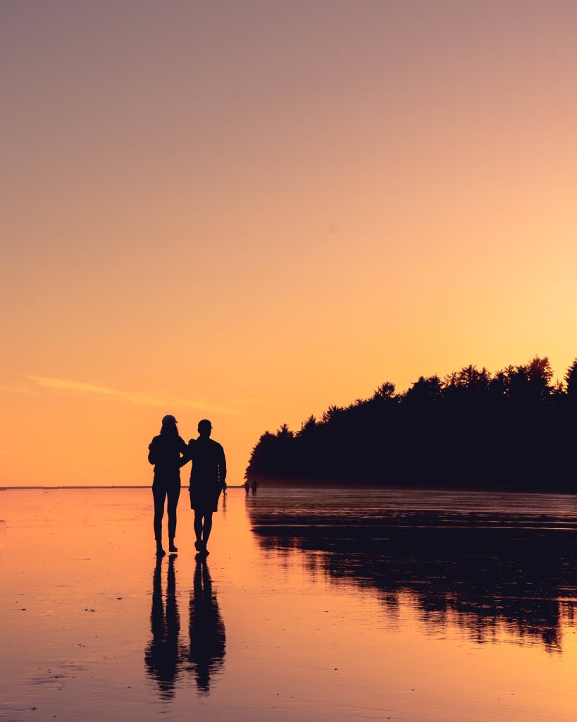 Couple walking arm-in-arm on reflective beach at sunset romantic peaceful wallpaper background