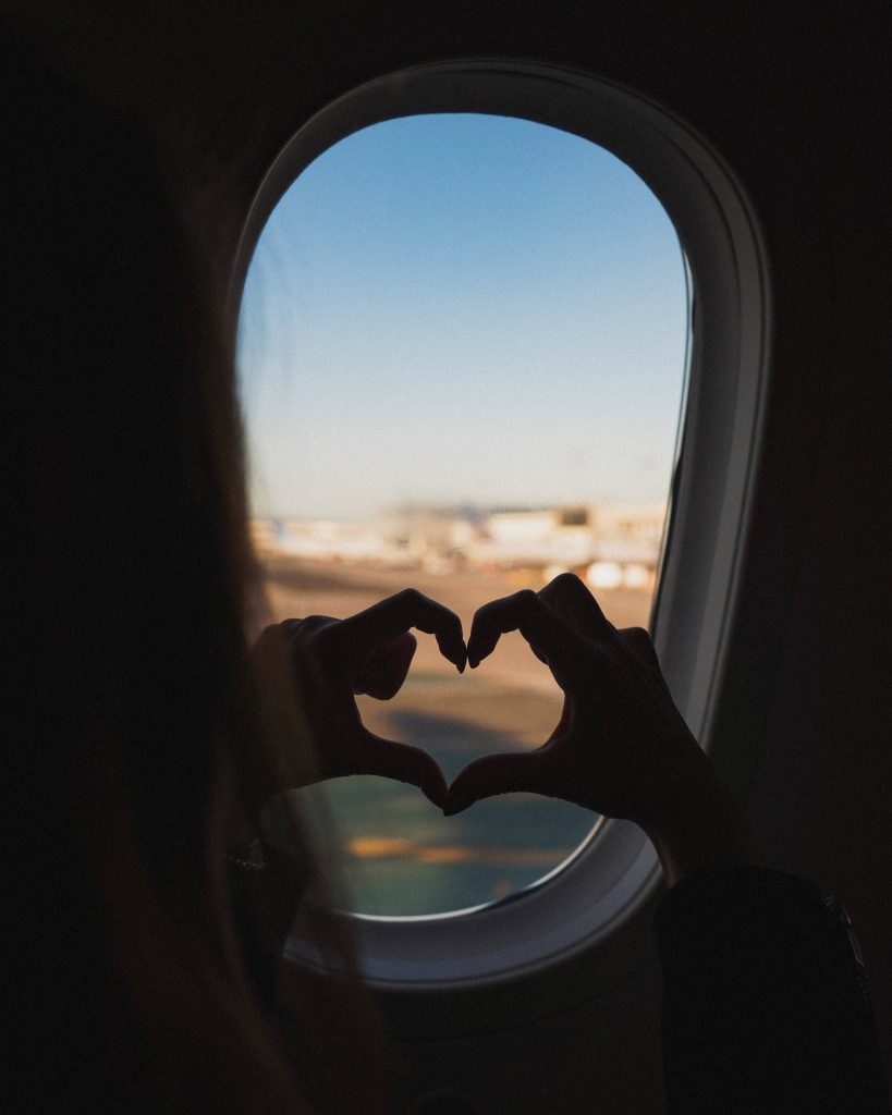 Hands forming heart shape silhouette on airplane window with runway and clear sky view wallpaper