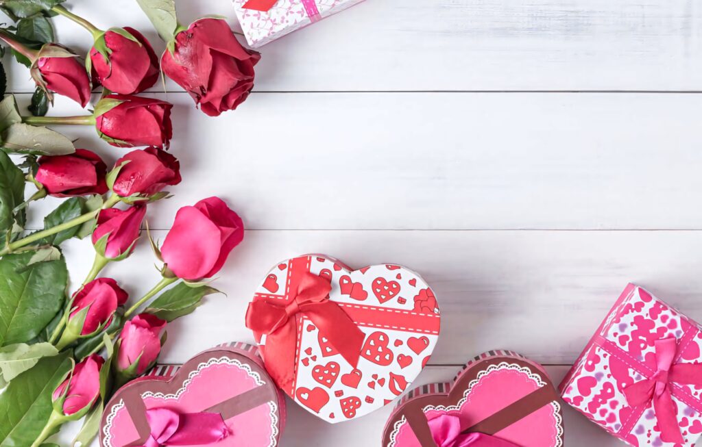 Valentines Day heart shaped gift boxes with red ribbons and fresh red roses on white wood Wallpaper