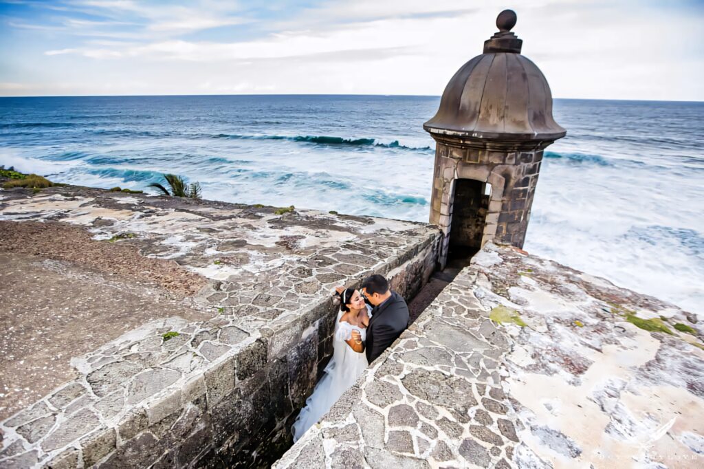 Romantic wedding photo of couple embracing at Castillo San Felipe del Morro with ocean waves background Wallpaper