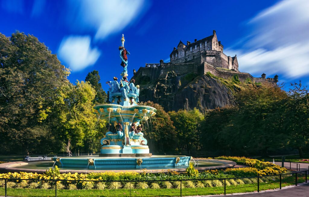 Ross Fountain in Edinburgh with castle backdrop bright sky lush greenery and vivid flowers wallpaper