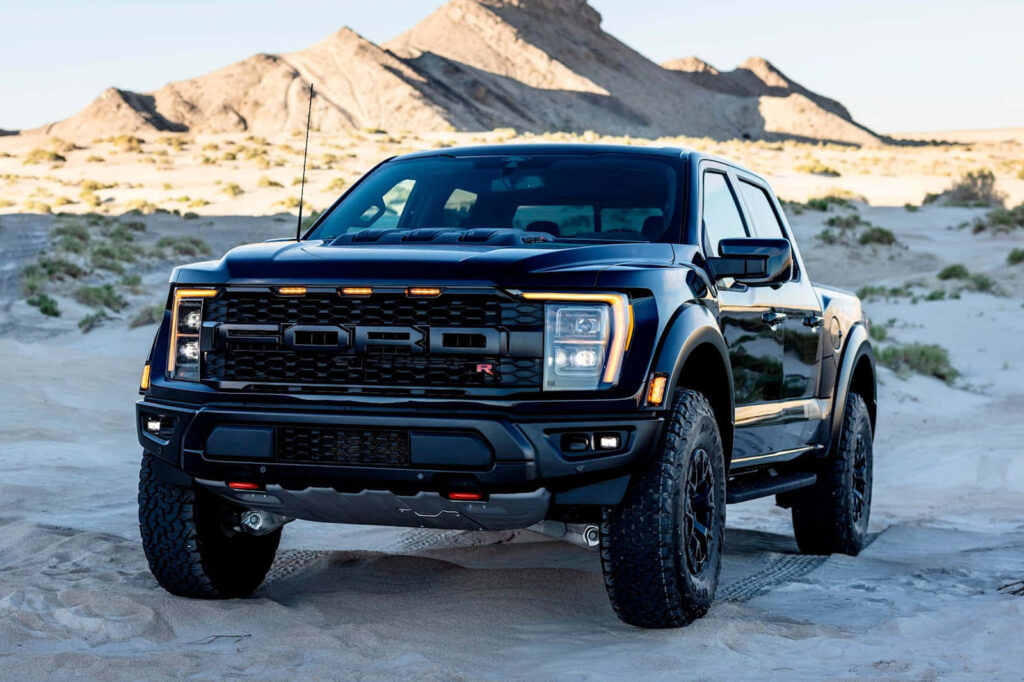 Black Ford F150 Raptor parked on sunlit desert sand with rocky formations background wallpaper