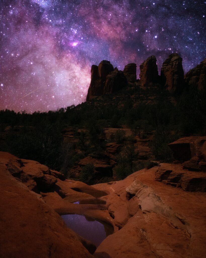 Starry night sky over rugged canyon rocks with vivid purples and deep blues of Milky Way Wallpaper