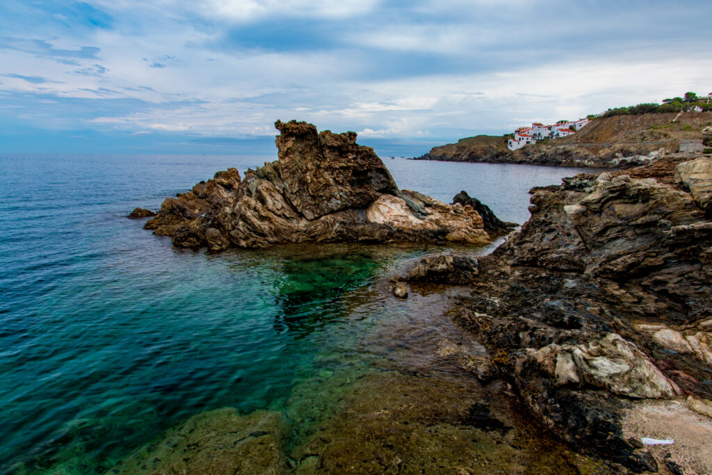 Rugged coastline with rocky cliffs turquoise sea and white seaside houses under cloudy sky wallpaper