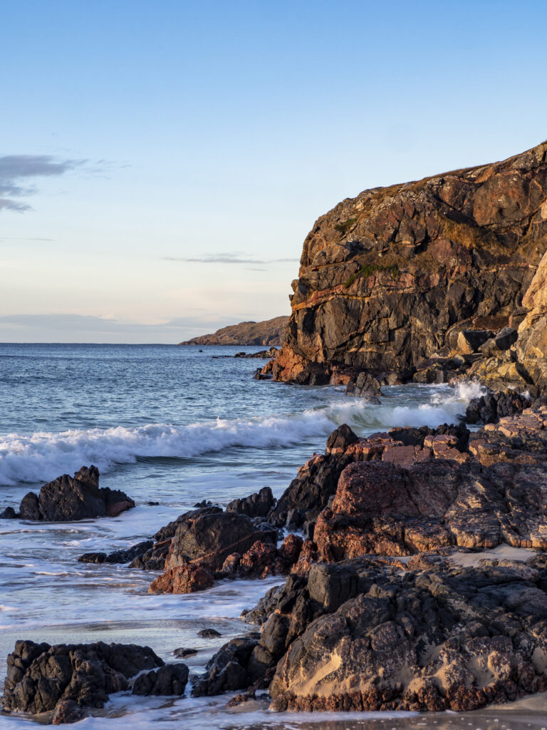 Rugged coastal landscape with jagged rocks and rolling sea waves under clear blue sky wallpaper