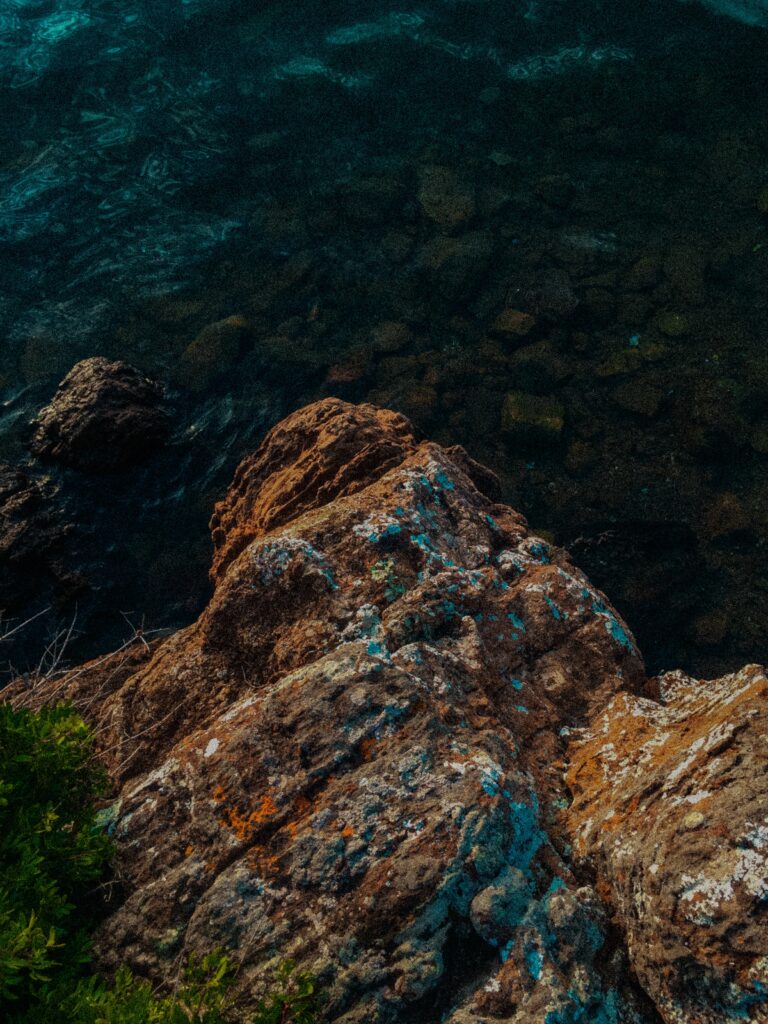 Rugged coastal rocks by clear blue green sea water meeting shore natural serene landscape wallpaper