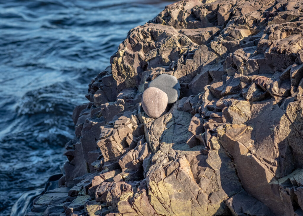 Rugged coastal rocks against deep blue sea waves with natural textures and earthy tones wallpaper