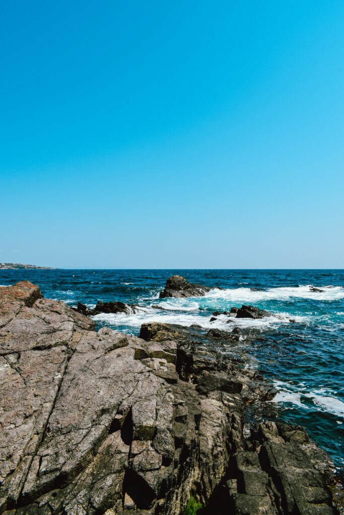 Rugged coastal rocks and wavy sea waters under clear blue sky natural scenic wallpaper background