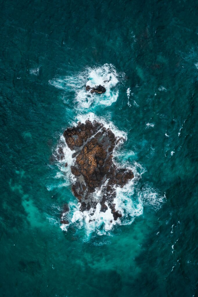 Aerial view of rugged rocks with white foam in vibrant blue ocean waves wallpaper background