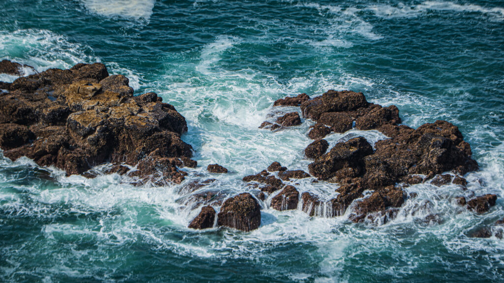 Rugged coastal rocks with swirling white sea foam and dynamic ocean waves wallpaper background