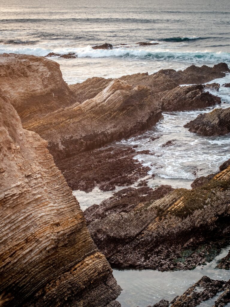 Rugged coastal rocks with gentle waves in earthy browns and serene blue sea wallpaper background