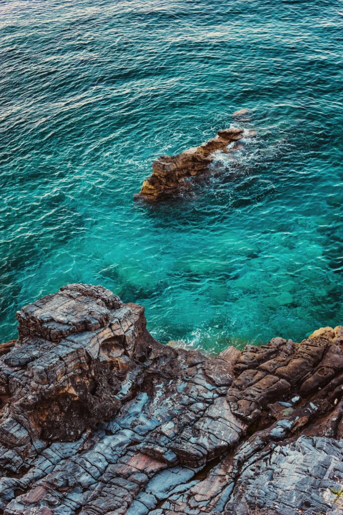 Aerial view of rugged rocky coastline meeting vibrant blue-green clear sea water wallpaper background
