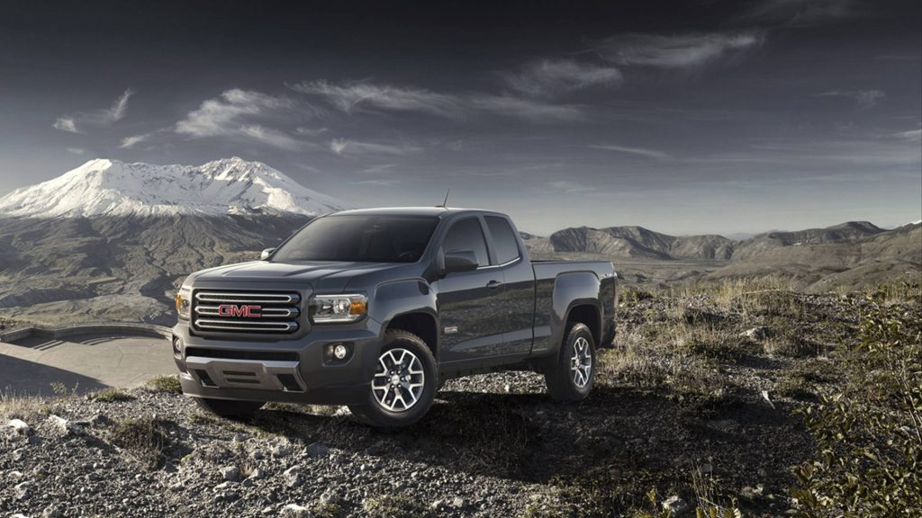 Grey GMC Canyon pickup on rocky ridge with snow-capped volcano and moody sky background wallpaper