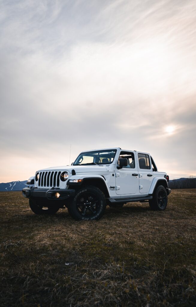 Adventure Awaits: Jeep Wrangler in Open Field Under Cloudy Sky Wallpaper