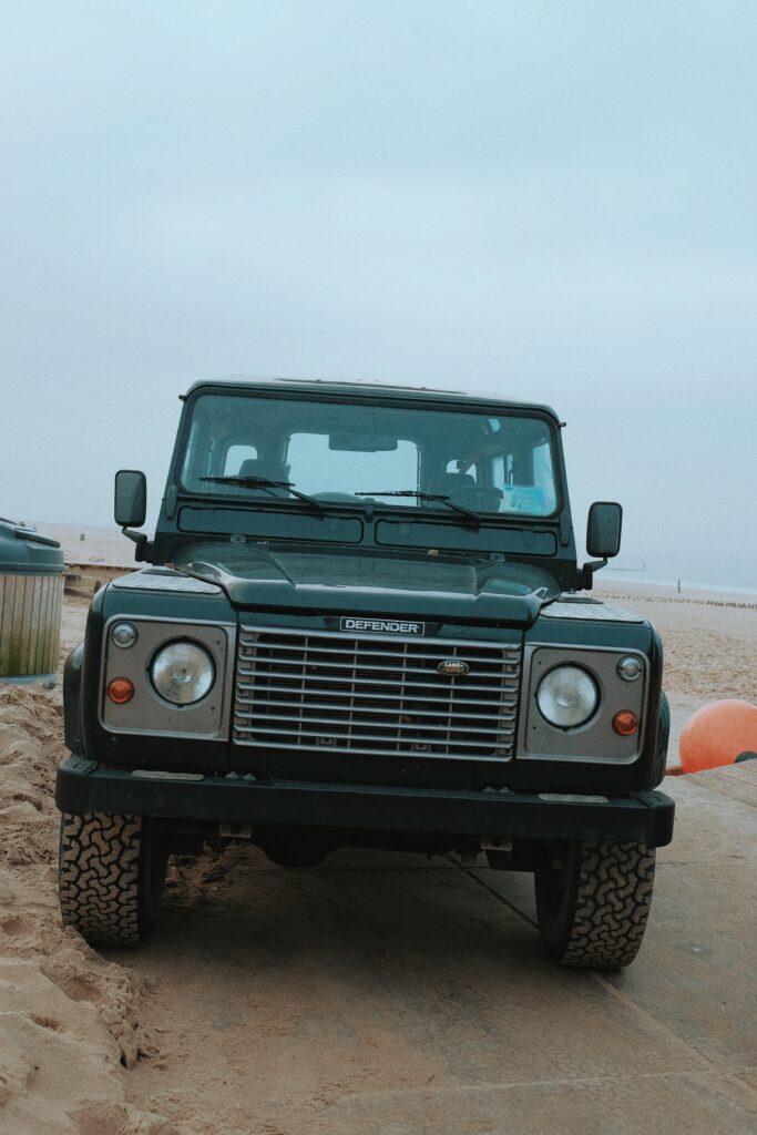 Front View of Rugged Land Rover Defender Against Sand and Sky Background Wallpaper