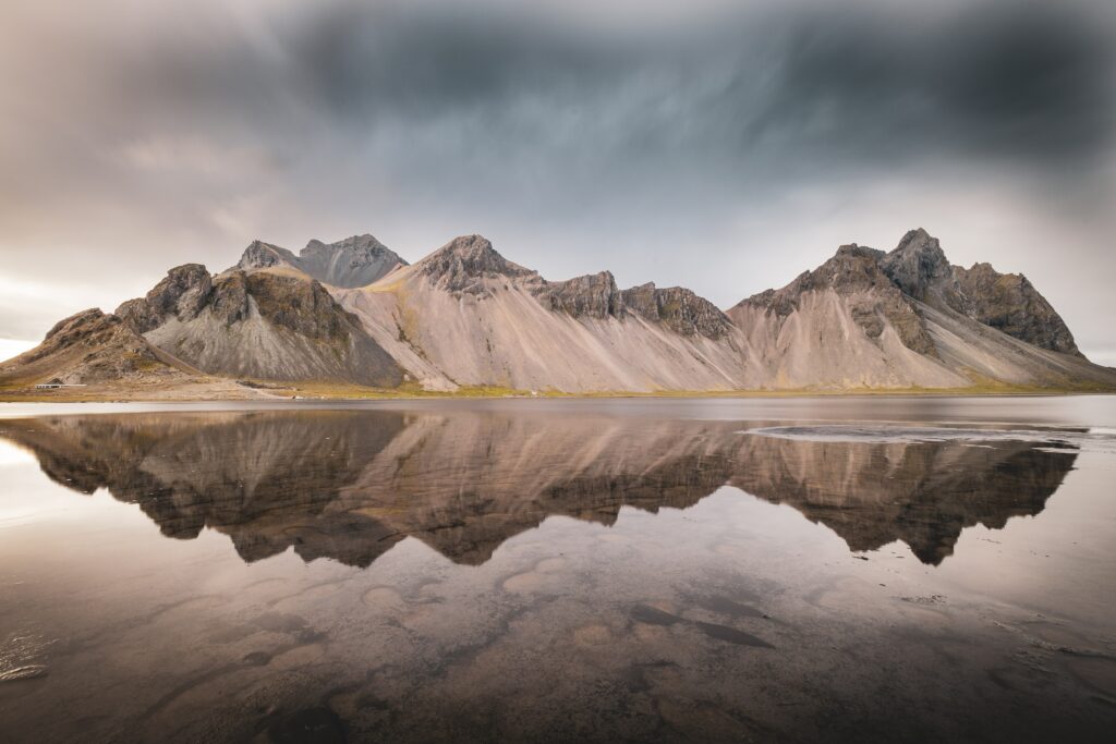 Rugged mountains reflected in calm lake under dramatic overcast sky earthy tones landscape wallpaper