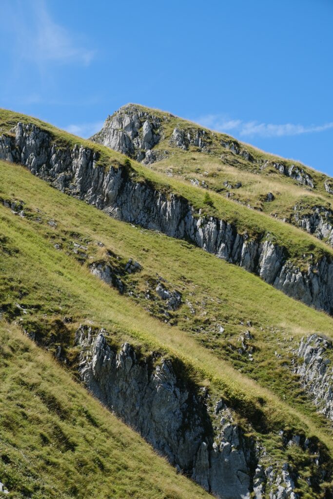 Rugged mountain slope with green grass and sharp rocks under clear blue sky nature wallpaper