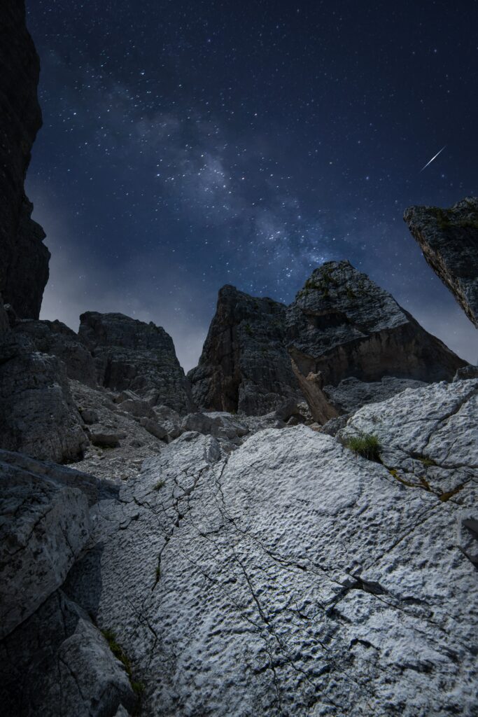 Starry night sky over rugged mountains and textured rocks with a meteor streaking above Wallpaper
